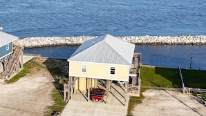 A waterfront property with a single-story building, a covered carport, and a small dock. - Bay Views at The Anchor Holds - formally Overboard (Grand Isle)
