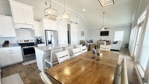A spacious kitchen with white cabinetry, a large wooden dining table, and modern appliances. - Bay Views at The Anchor Holds - formally Overboard (Grand Isle)