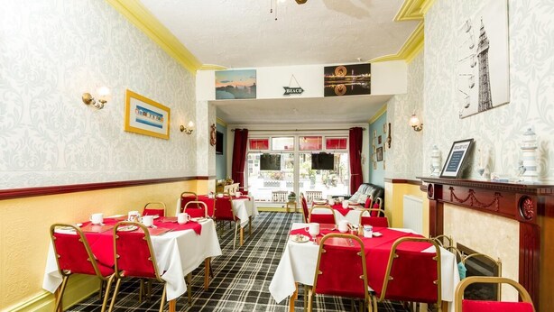 A dining area with red and white tables and chairs, a checkered floor, and a view through a window to the outside. - Valdene Hotel (Blackpool)