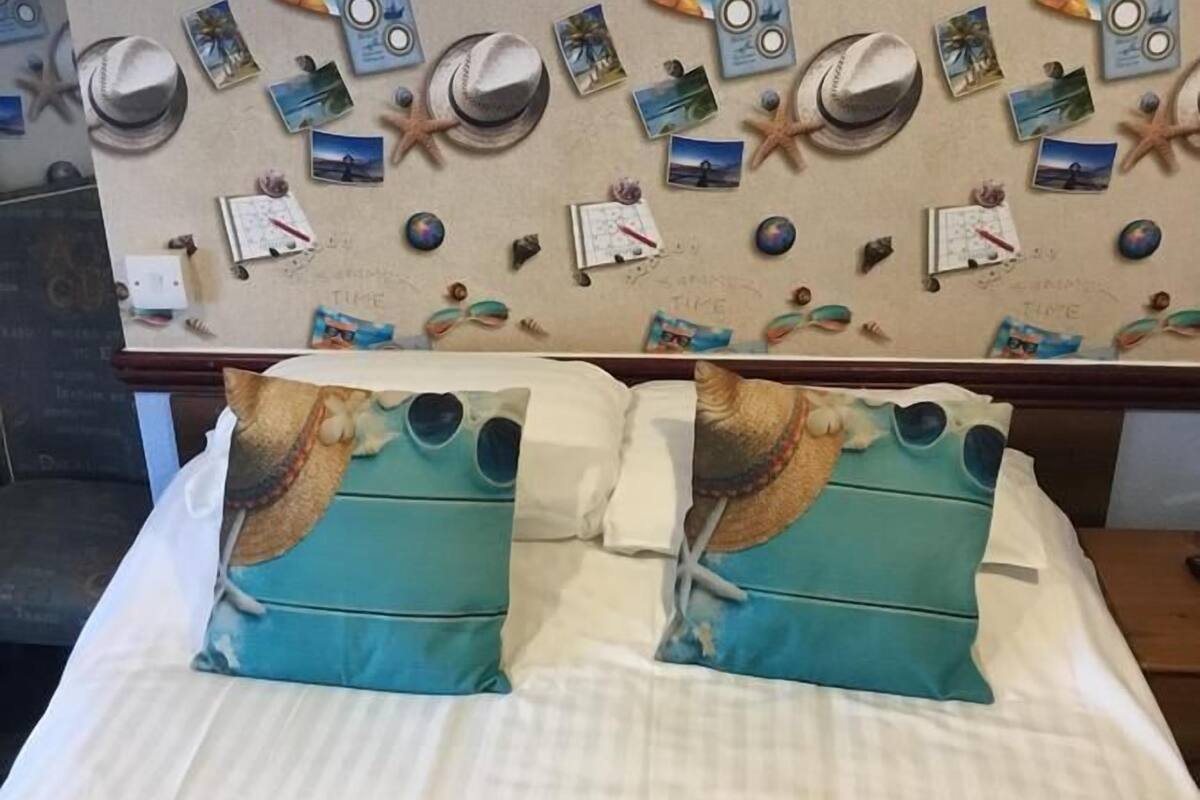 Egy ágy két párnával, melyek tengerparti motívumot ábrázolnak, egy fal, melyen fényképek és tengericsillagok mintája látható, és egy naptár.
