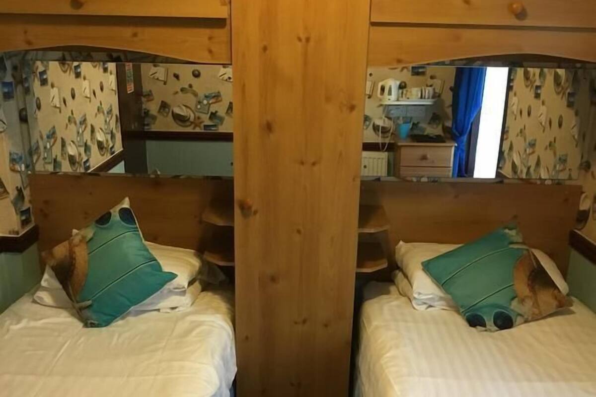 Egy szoba, amelyben két ágy található, mindkettőnek fafejtámlája van, és egy központi, fa ajtó vezet be.