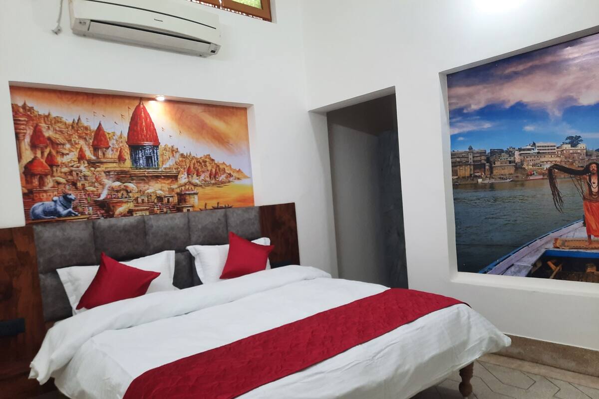 A hotel room with a bed, a painting of a cityscape, and an air conditioning unit.