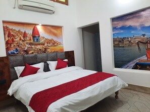A hotel room with a bed, a painting of a cityscape, and an air conditioning unit.