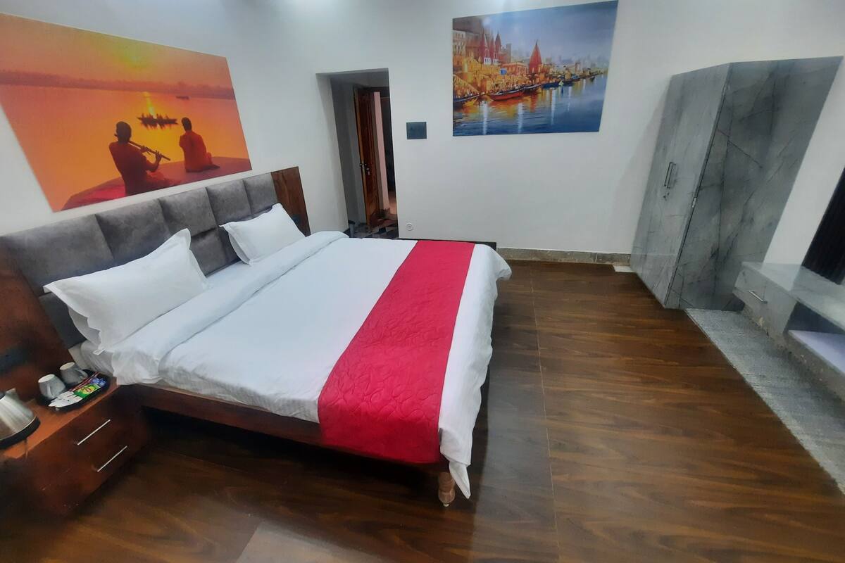 A hotel room with a large bed, wooden flooring, a nightstand, and two paintings on the walls.