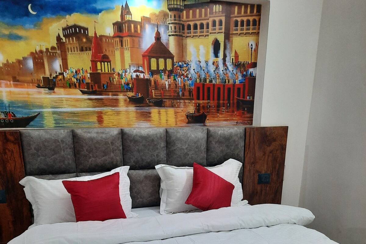 A bed with white and red bedding, a grey upholstered headboard, and a red throw blanket.
