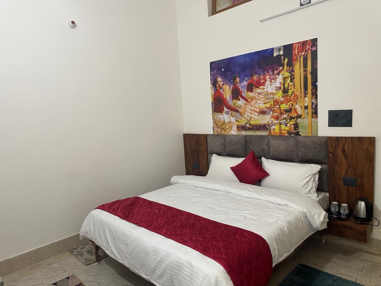 Un dormitorio con cama, cabecera, mesita de noche y un cuadro colgado en la pared.