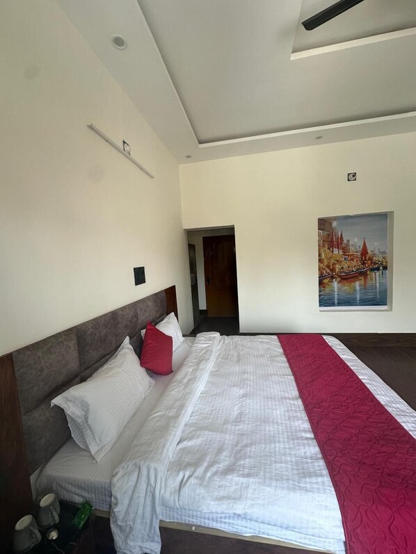 A modern hotel room with a large bed, a headboard, a painting on the wall, and a ceiling fan.
