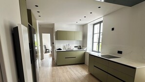 Une cuisine moderne avec un plancher en bois clair, des armoires vertes et une grande fenêtre.