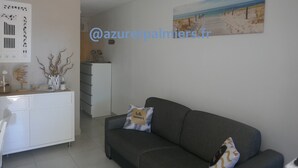 A modern living room with a grey sofa, a white cabinet, and a painting of a beach scene. - 50m sandy beach. All comforts ***. Quiet - Private parking - Air-conditioned (Hyères)