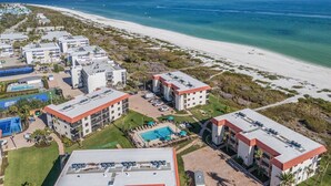 An aerial view of a coastal hotel with multiple buildings, a beach, and a swimming pool.