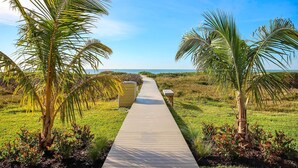 A wooden pathway leading to a beach with palm trees on either side.