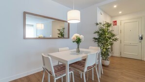 A dining area with a white table, four chairs, a vase with flowers, a hanging light fixture, and a potted plant.
