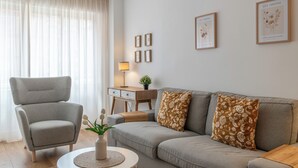 A modern living room with a grey sofa, a grey armchair, a small round table with a vase of flowers, and a lamp on a wooden side table.