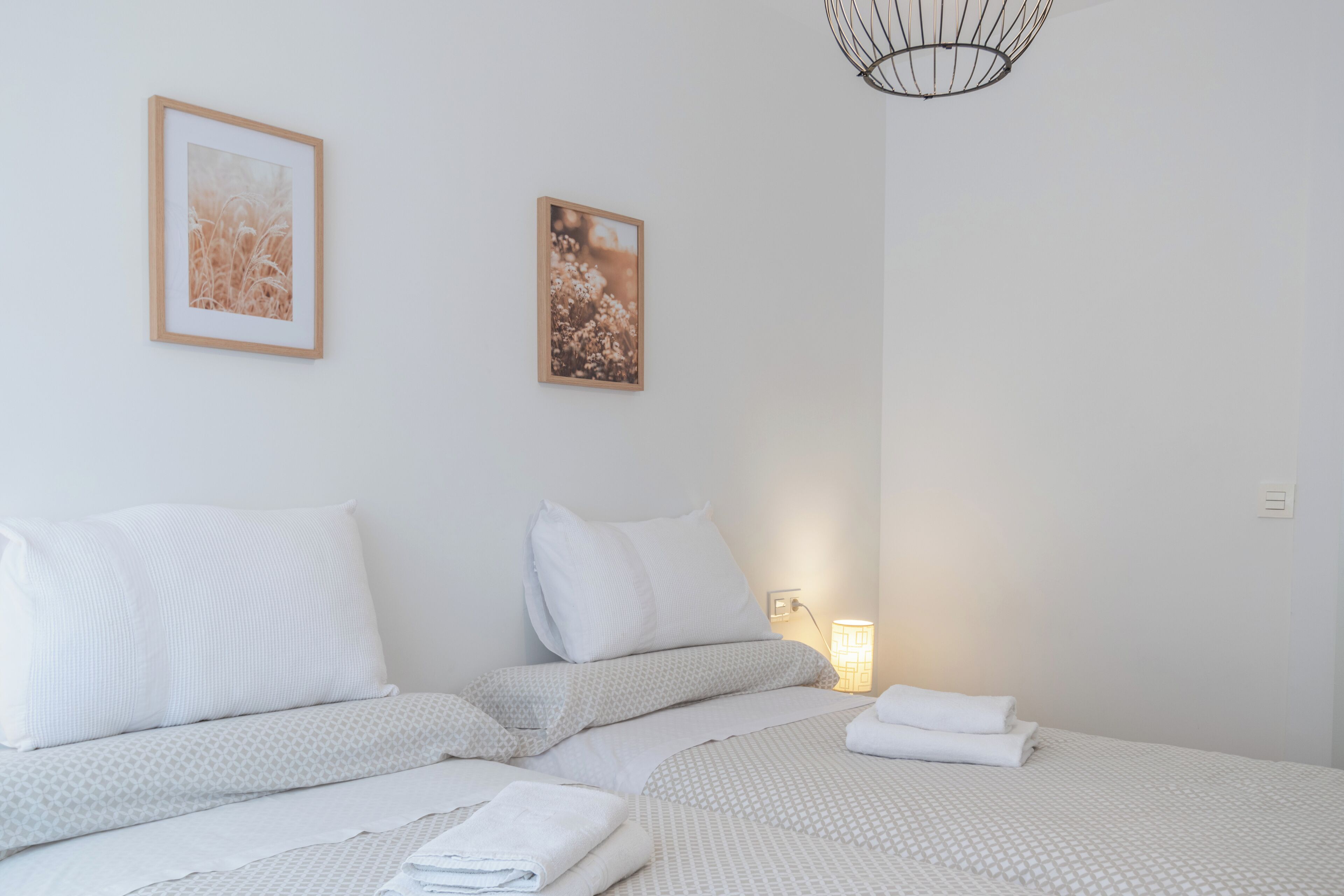 Une chambre d’hôtel avec deux lits, du linge de lit blanc et deux tableaux encadrés au mur.