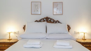 A neatly made bed with white linens, two framed artworks on the wall, and bedside lamps on wooden nightstands.