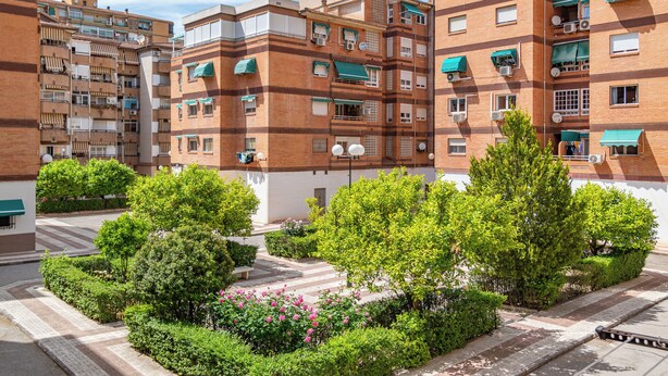 A multi-story residential building with balconies, air conditioning units, and a courtyard with greenery and a pathway.