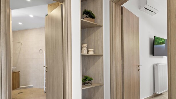 Une salle de bain moderne équipée d’une douche, de toilettes et d’un lavabo. On y trouve des portes en bois, un téléviseur fixé au mur et un radiateur.