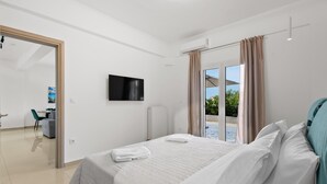 Une chambre d’hôtel moderne équipée d’un lit, d’une télévision, d’une porte-fenêtre coulissante donnant sur un balcon et d’un petit espace bureau.