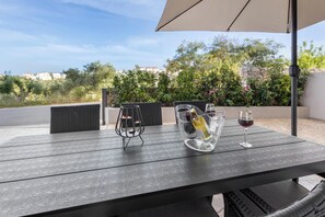 An outdoor patio with a table, wicker chairs, and a wine bottle and glass. - Palea Luxury Living (Chania)