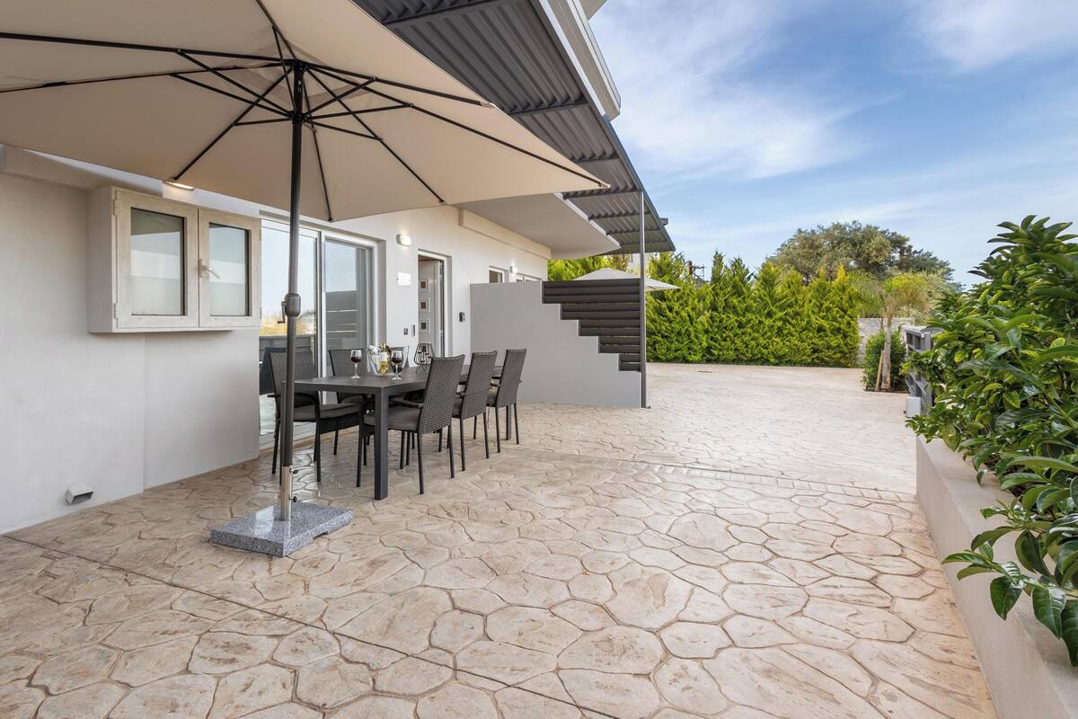 An outdoor patio with a dining table and chairs, a large umbrella, and a stone-tiled floor.