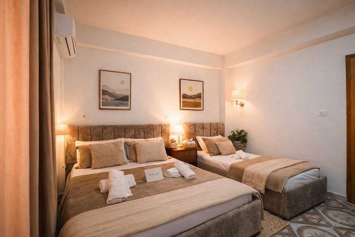 A hotel room with two beds, a nightstand, wall-mounted lamps, and two framed pictures.