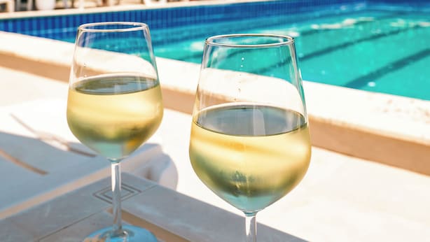 Two glasses of white wine on a poolside table with a clear blue pool and lounge chairs in the background. - KURTI Hotel (Golem)