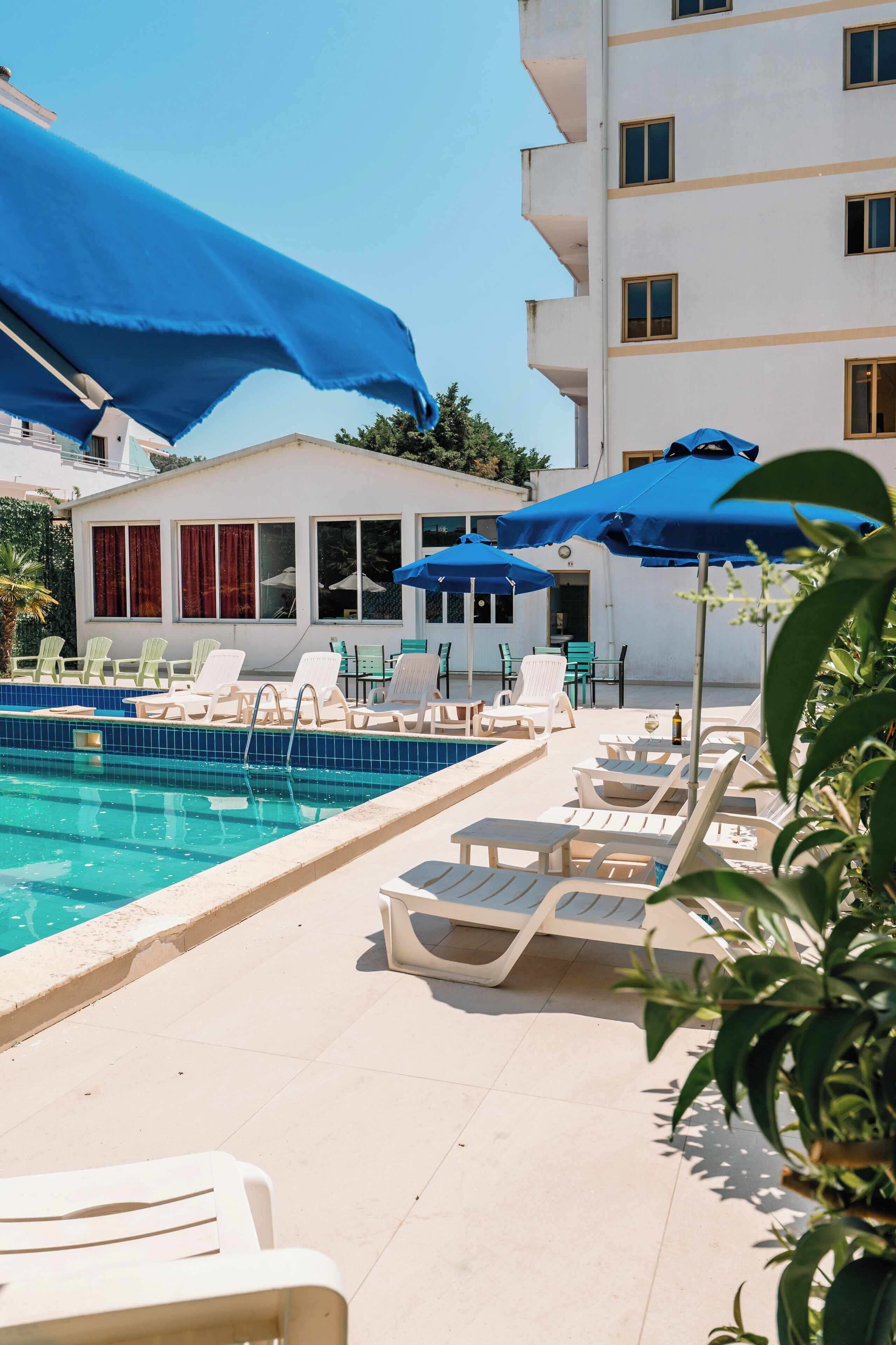 A pool area with lounge chairs and blue umbrellas, surrounded by a white building with multiple windows.