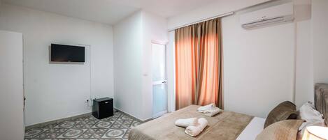 A hotel room with two beds, a television, an air conditioning unit, and patterned floor tiles.
