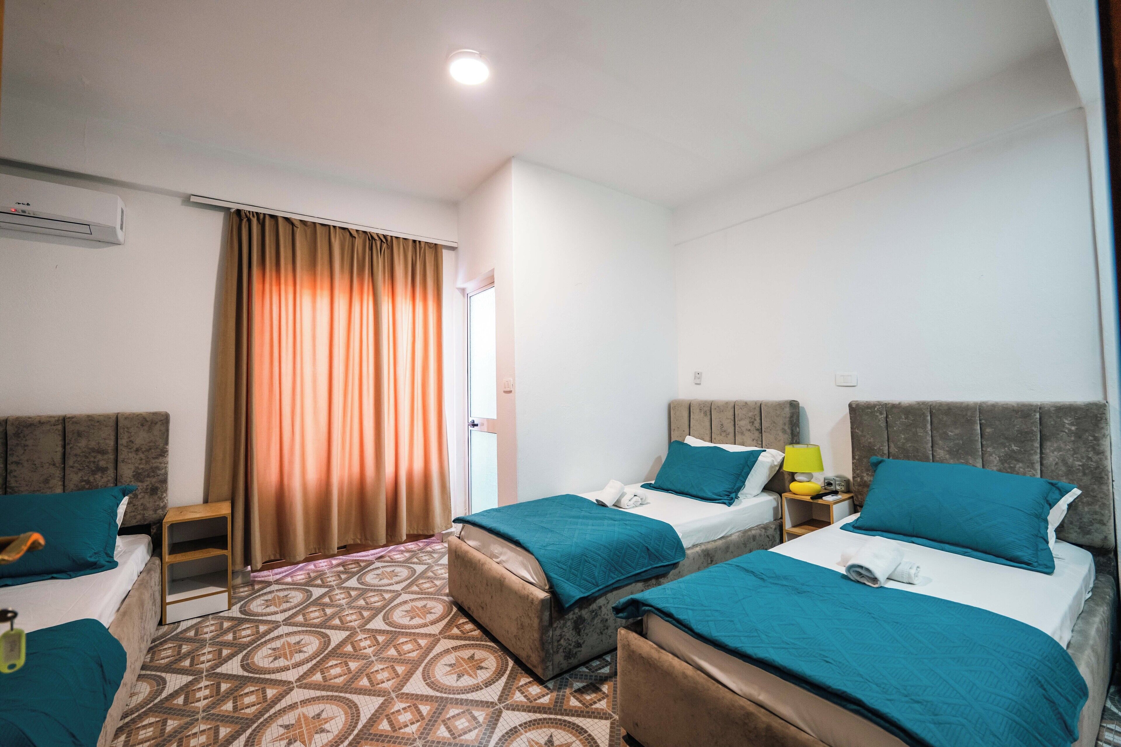 Ein Hotelzimmer mit zwei Betten, einem kleinen Tisch, einem Stuhl, einer Klimaanlage und einem gemusterten Teppich.