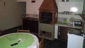 A compact kitchen with a brick oven, a sink, and a small refrigerator. - Fully furnished studio apartment 300 meters from Juréia beach.   (Iguape)