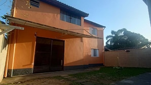 A two-story building with a flat roof, a covered entrance, and a small garden area. - Fully furnished studio apartment 300 meters from Juréia beach.   (Iguape)