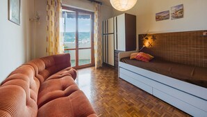 Un salon moderne avec un canapé, un lit, un plancher en bois, une grande fenêtre et un luminaire suspendu.