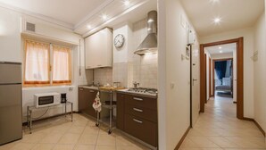 Une cuisine équipée d’un four à micro-ondes, d’une cuisinière et d’un four traditionnel. Il y a une horloge au mur et une fenêtre avec des rideaux.