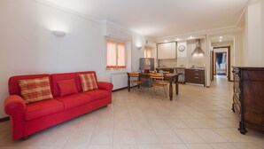 Un vaste espace de vie comprenant un canapé rouge, une table à manger et une cuisine en arrière-plan.