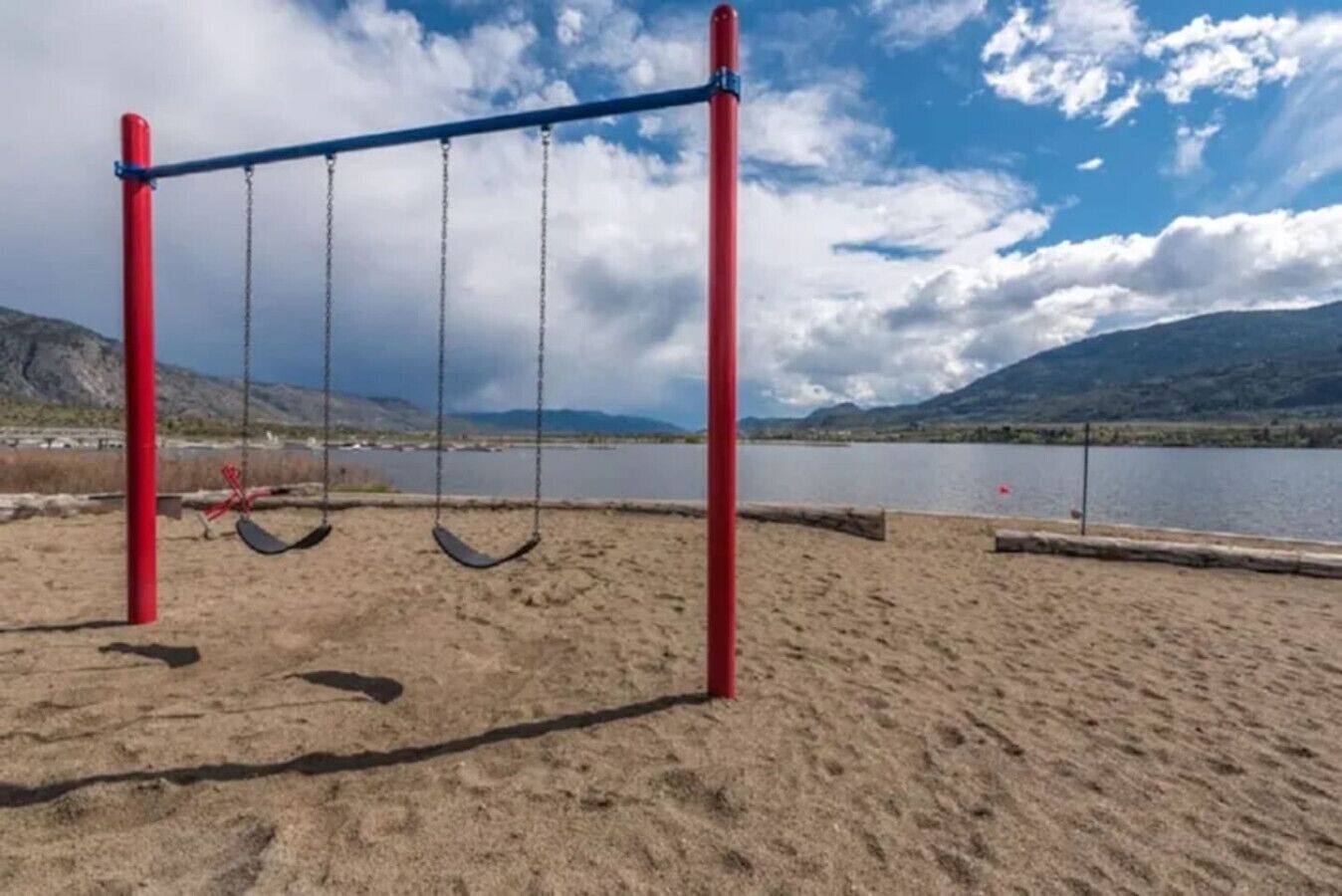 A beach with a swing set and a lake in the background.