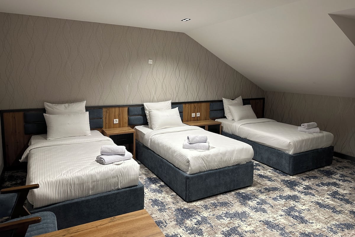 Habitación de hotel con tres camas dispuestas en fila, cada una con cabecero de madera y ropa de cama blanca.
