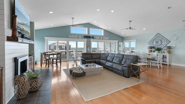A spacious living room with a fireplace, a sectional sofa, and a dining area with white furniture. - Enjoy ocean views in "The Good Life" on Oak Island, featuring 5BR, private pool, and room for 17. (Oak Island)