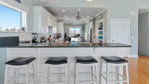 A spacious kitchen with a large island, white cabinetry, and bar stools. - Enjoy ocean views in "The Good Life" on Oak Island, featuring 5BR, private pool, and room for 17. (Oak Island)