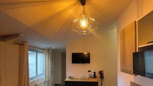 A modern dining area with a wooden table and chairs, a hanging light fixture, a television mounted on the wall, and a window with curtains. - Tarascon center apartment (Tarascon)