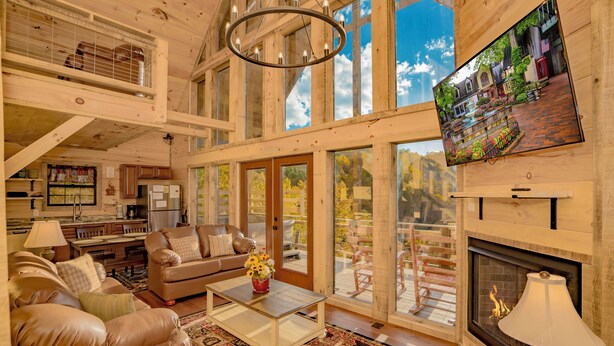 A spacious living room with a fireplace, a television mounted on the wall, and a balcony with outdoor furniture. - 🌲 Paradise View In The Smokies 🌅 Views, Resort Pool & Game Room (Sevierville)