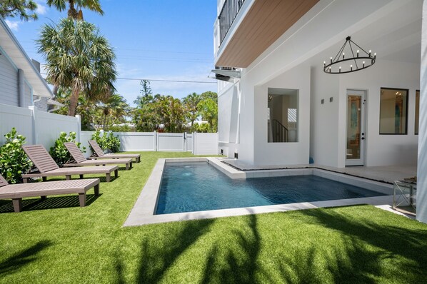 Zona de piscina exterior moderna amb un edifici blanc, un porxo cobert i gandules.