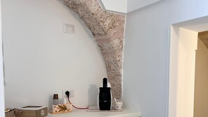 A small kitchen with a white countertop, a coffee maker, and a kettle. There is a window with a stone arch design above the counter. - Trullo in Light Standard (Alberobello)