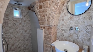 A bathroom with a stone wall, a white sink, a mirror, and a small window. - Trullo in Light Standard (Alberobello)