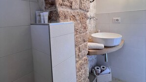 A bathroom with a stone wall, a white sink, a mirror, and a towel rack. - Trullo in Light Standard (Alberobello)