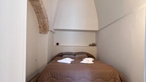 A narrow, vaulted room with a bed, a stone wall, and a white ceiling. - Trullo in Light Standard (Alberobello)
