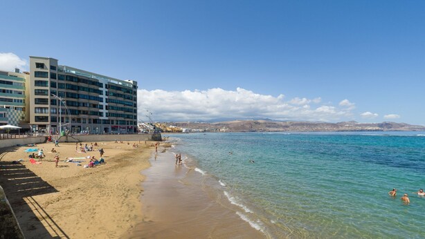 A beach with clear water, a hotel, and people swimming.
