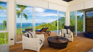 Un salon moderne doté de grandes portes vitrées donnant sur un balcon avec vue sur l’océan et les palmiers.