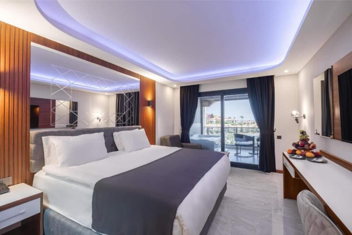 A modern hotel room with a large bed, a desk, a chair, and a balcony with a view.