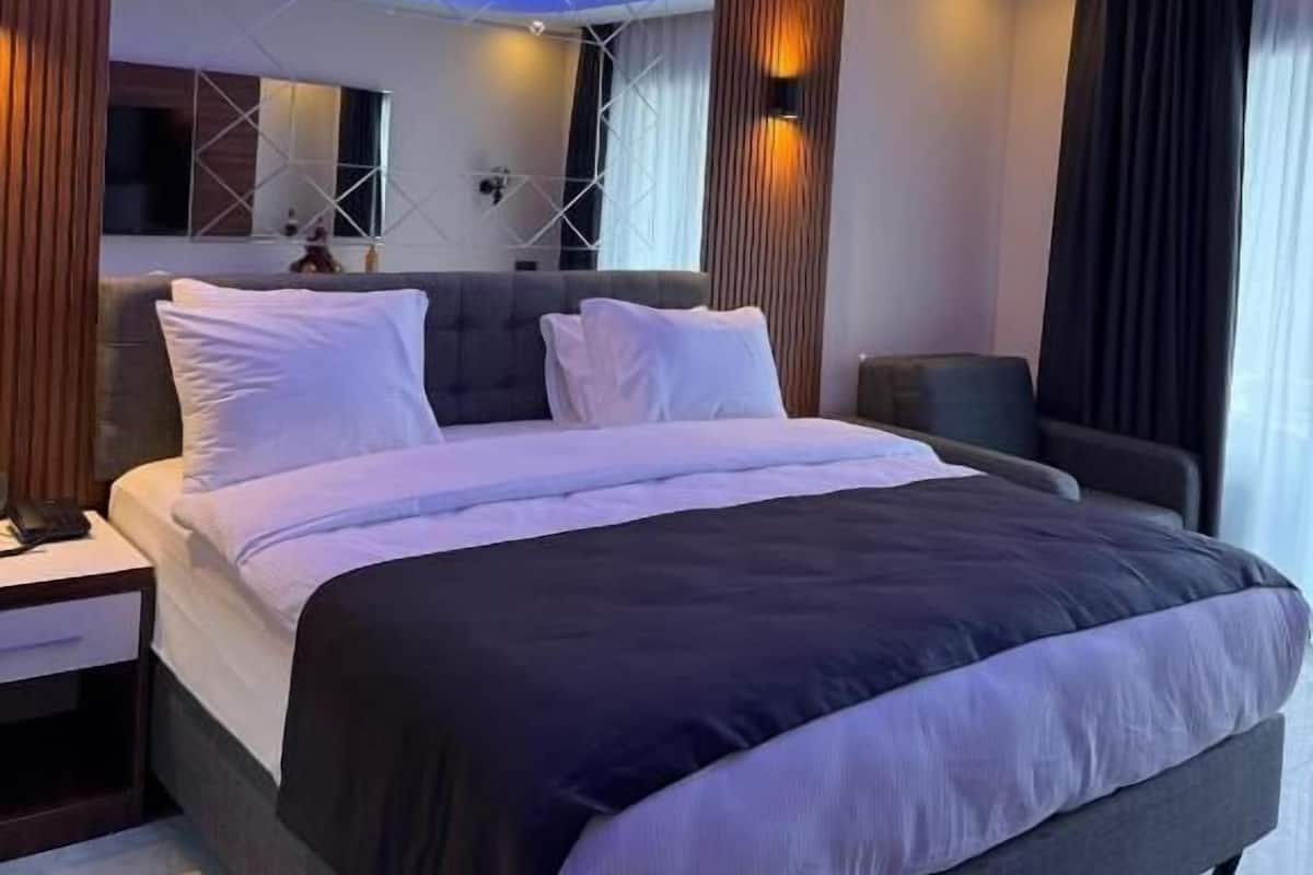 A modern hotel room with a large bed, a nightstand, a bedside table, and a wall-mounted TV.