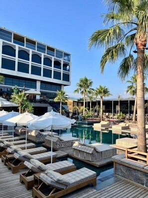 Un resort con piscina, sillones de descanso, sombrillas y palmeras.